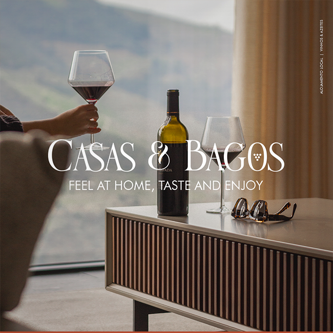 Casas e Bagos, design com fotografia de sala de estar, pessoa a segurar copo de vinho, mesa com mais um copo, garrafa e óculos de sol. Na frente o logo e o slogan 'Feel at Home, Taste and Enjoy'
